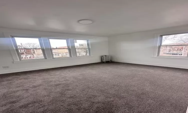 Unfurnished room featuring radiator, baseboards, and dark carpet