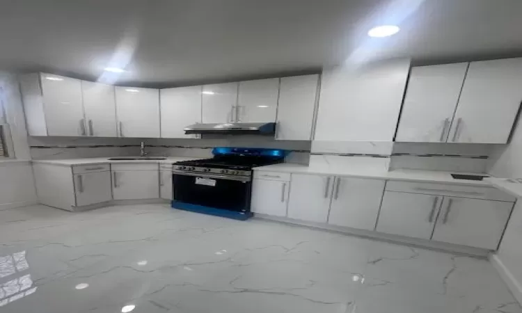 Kitchen with stainless steel gas stove, marble finish floor, light countertops, and under cabinet range hood