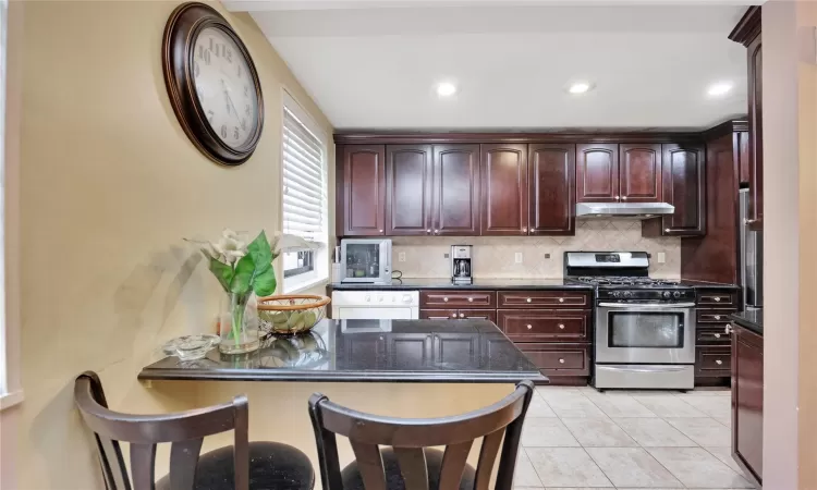 Kitchen featuring under cabinet range hood, dishwashing machine, backsplash, and stainless steel gas range