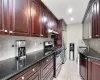 Kitchen with dark stone counters, light tile patterned flooring, under cabinet range hood, appliances with stainless steel finishes, and backsplash