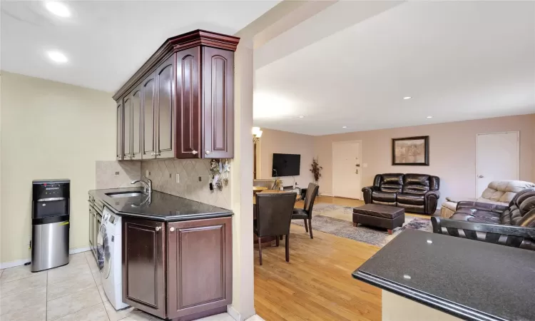 Kitchen featuring a sink, tasteful backsplash, dark countertops, open floor plan, and washer / dryer