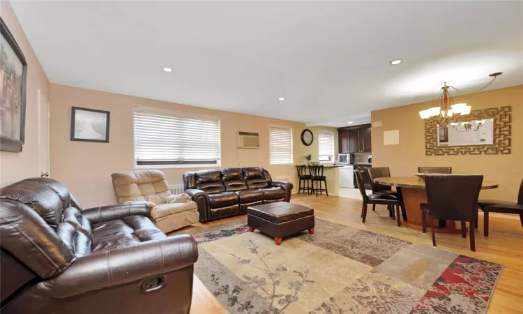 Living room with recessed lighting, a wall mounted air conditioner, an inviting chandelier, and light wood-style flooring