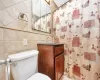 Full bath with curtained shower, toilet, tile walls, and vanity