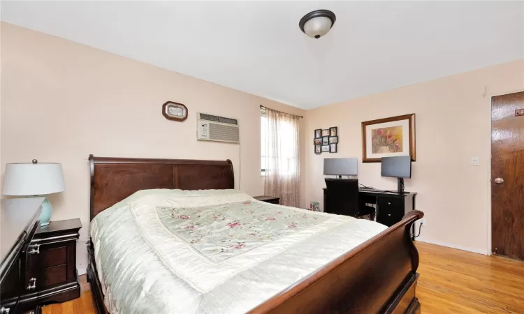 Bedroom with light wood finished floors, a wall mounted AC, and baseboards