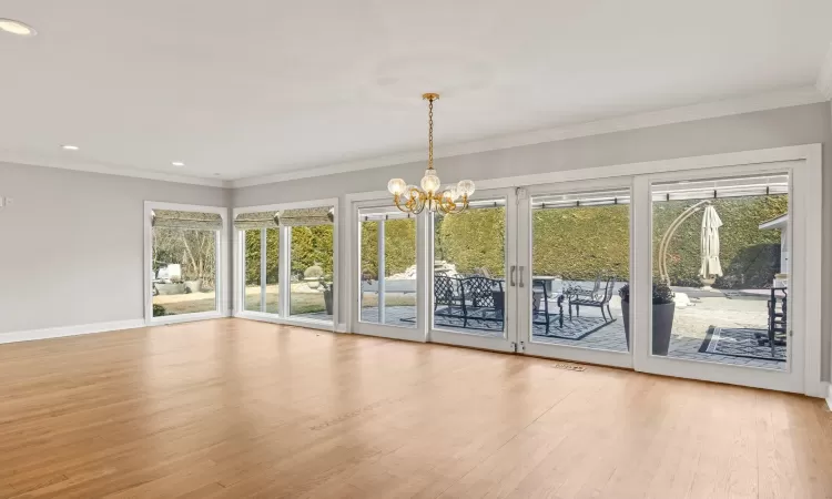 Unfurnished living room with a notable chandelier, a healthy amount of sunlight, wood finished floors, and crown molding