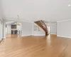 Unfurnished living room featuring baseboards, light wood finished floors, an inviting chandelier, stairs, and crown molding