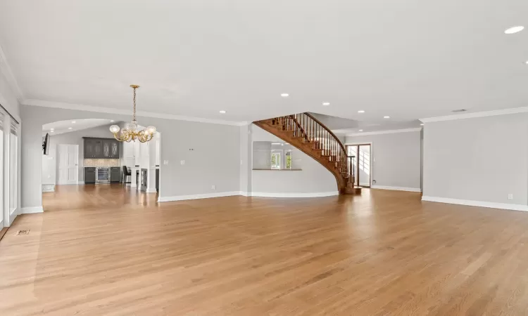 Unfurnished living room featuring baseboards, light wood finished floors, an inviting chandelier, stairs, and crown molding