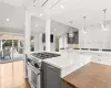 Kitchen with vaulted ceiling, wood finished floors, high end range, white cabinetry, and ornate columns