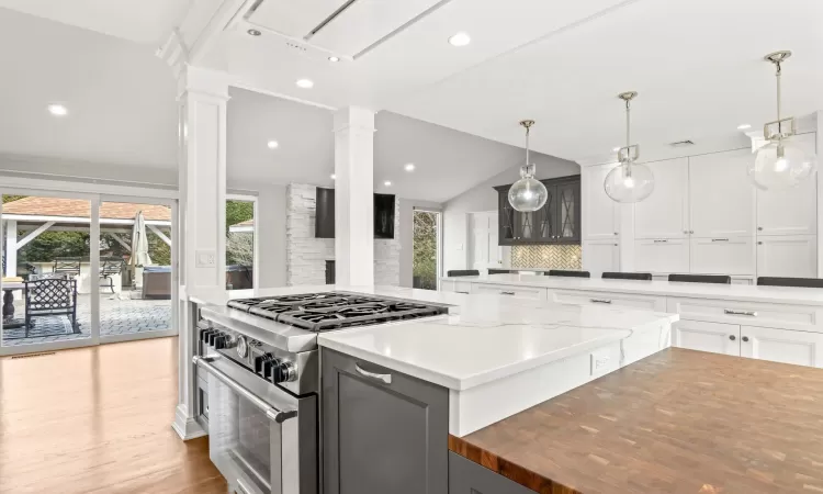 Kitchen with vaulted ceiling, wood finished floors, high end range, white cabinetry, and ornate columns