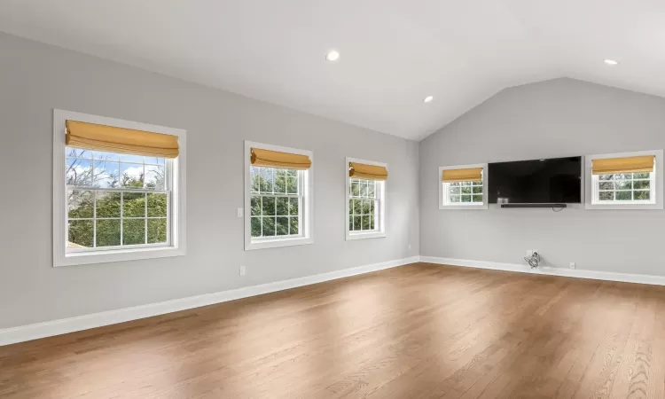 Unfurnished living room with recessed lighting, baseboards, lofted ceiling, and wood finished floors