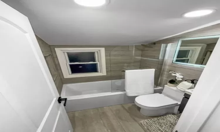 Bathroom with toilet, shower / bathtub combination, and wood finished floors