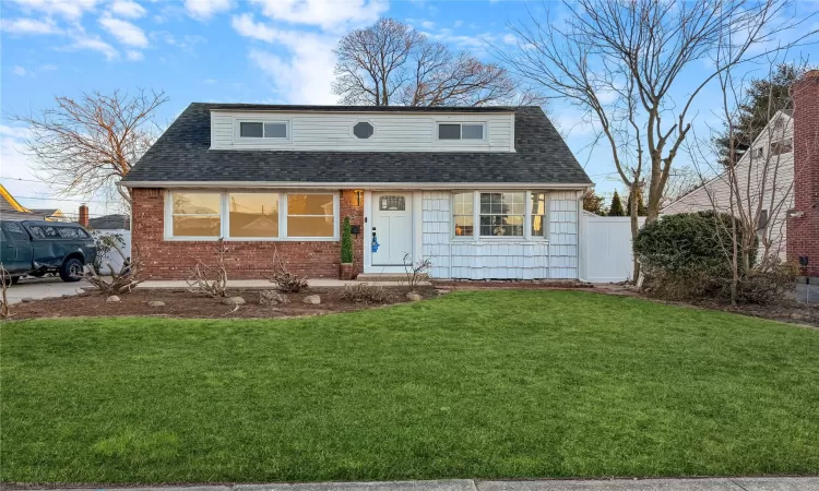 View of front of home featuring brick siding, a shingled roof, a front lawn, and fence