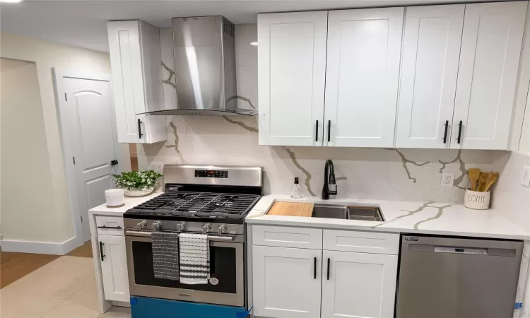 Kitchen featuring a sink, backsplash, white cabinetry, stainless steel appliances, and wall chimney exhaust hood