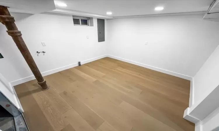 Finished basement featuring electric panel, baseboards, light wood-style flooring, and recessed lighting