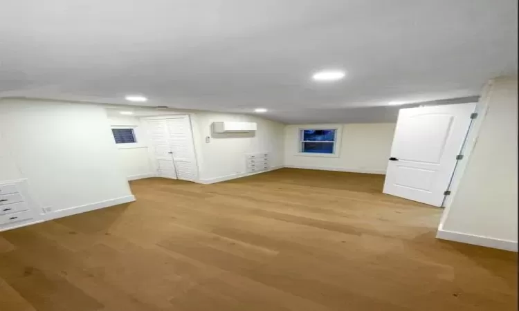 Finished basement with an AC wall unit, light wood-type flooring, and baseboards