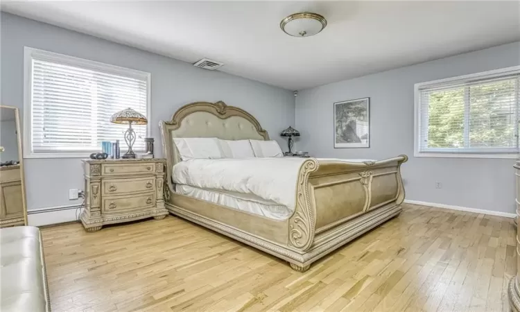 Bedroom with visible vents, light wood-style flooring, a baseboard heating unit, and baseboards