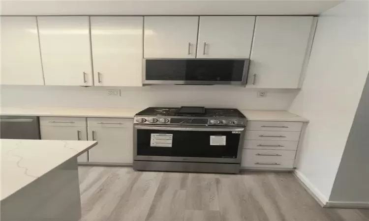 Kitchen with baseboards, light stone countertops, light wood-style flooring, stainless steel appliances, and white cabinetry