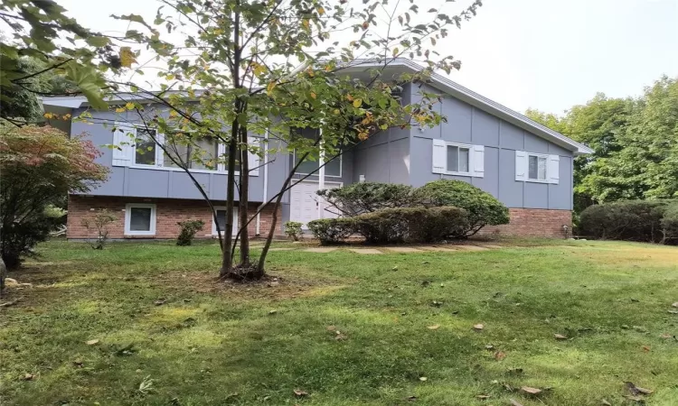 View of property exterior featuring board and batten siding, a lawn, and brick siding