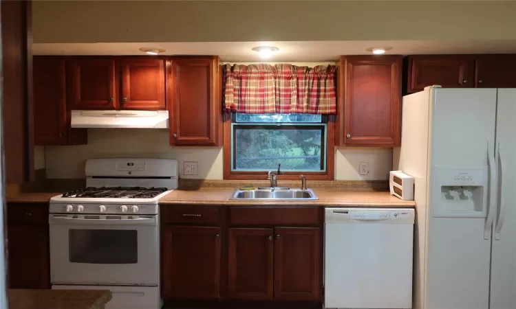 Kitchen featuring under cabinet range hood, white appliances, light countertops, and a sink