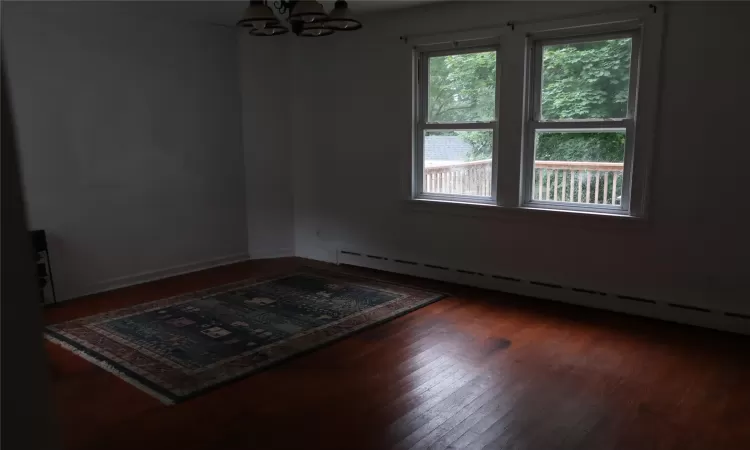 Unfurnished room with a notable chandelier, baseboard heating, and wood finished floors