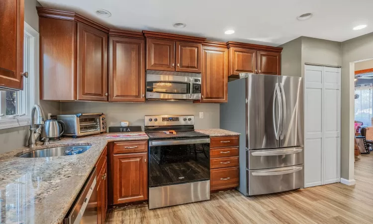 Kitchen with a toaster, light stone counters, light wood-style flooring, appliances with stainless steel finishes, and a sink