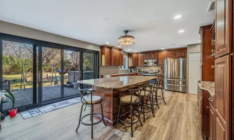 Kitchen with light stone counters, a kitchen island, appliances with stainless steel finishes, and a breakfast bar area