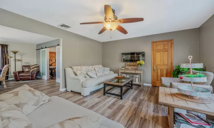 Living area featuring a ceiling fan, a barn door, wood finished floors, and visible vents