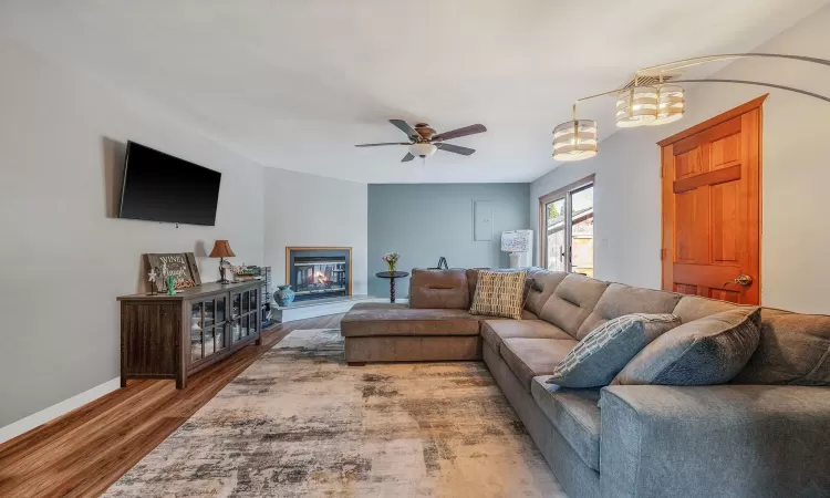 Living room with a glass covered fireplace, wood finished floors, baseboards, and a ceiling fan