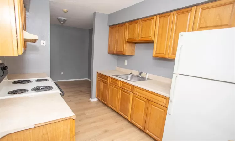 Kitchen with light countertops, range with electric stovetop, freestanding refrigerator, and a sink