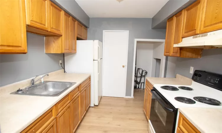 Kitchen with under cabinet range hood, electric range, light countertops, and a sink