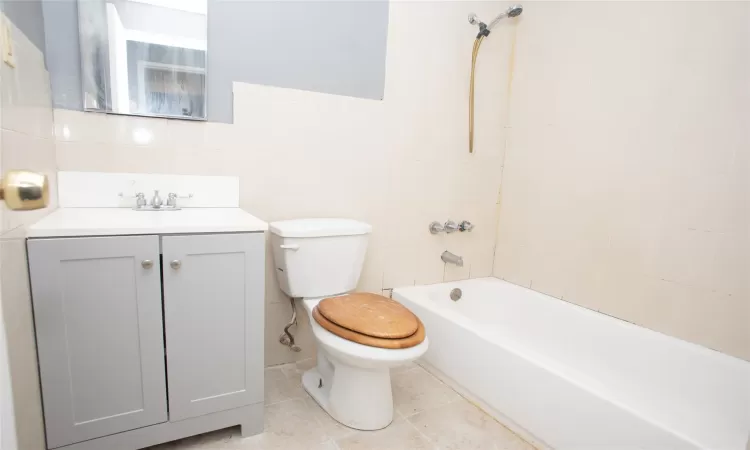 Full bath with tile patterned flooring, washtub / shower combination, toilet, vanity, and tile walls