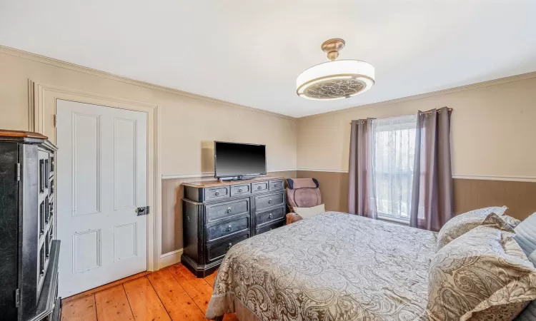 Bedroom with light wood finished floors, wainscoting, and crown molding