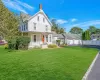 Victorian-style house with a front yard, driveway, a porch, a chimney, and a garage