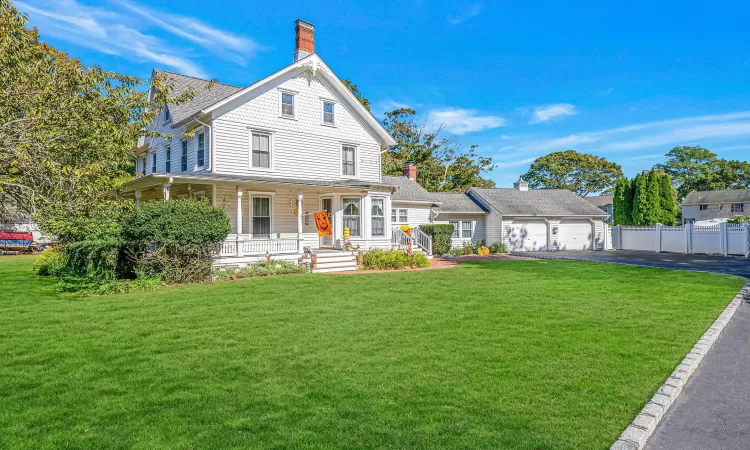 Victorian-style house with a front yard, driveway, a porch, a chimney, and a garage