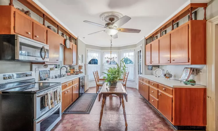 Kitchen with a sink, appliances with stainless steel finishes, crown molding, light countertops, and brick floor