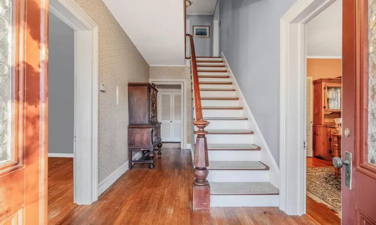 Stairs featuring baseboards, wood finished floors, ornamental molding, and wallpapered walls