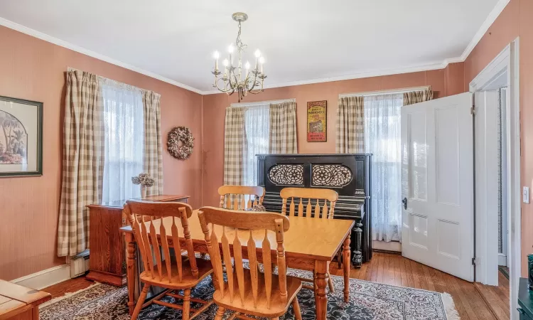 Dining area with baseboards, an inviting chandelier, light wood-style flooring, ornamental molding, and baseboard heating