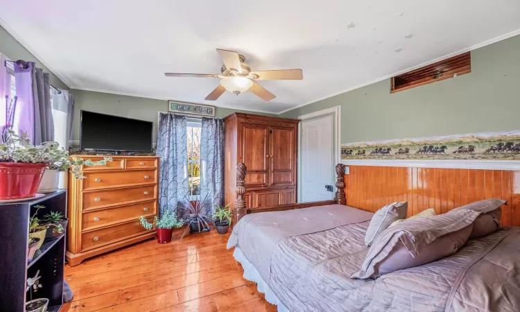 Bedroom featuring a wainscoted wall, a ceiling fan, light wood-style flooring, and crown molding