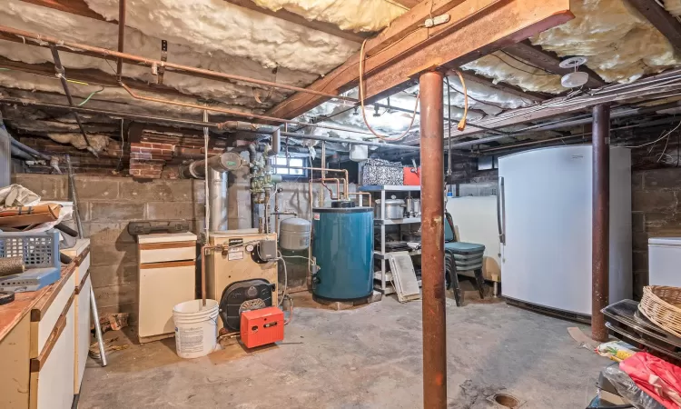 Unfinished below grade area featuring water heater, a heating unit, and freestanding refrigerator