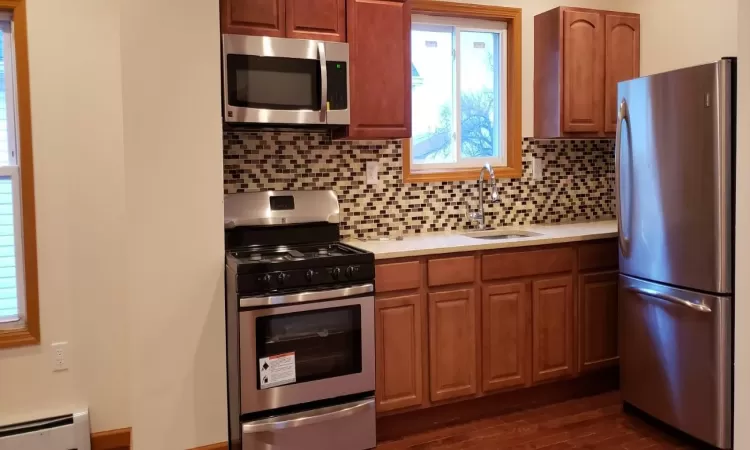 Kitchen featuring sink, baseboard heating, dark hardwood / wood-style floors, backsplash, and appliances with stainless steel finishes