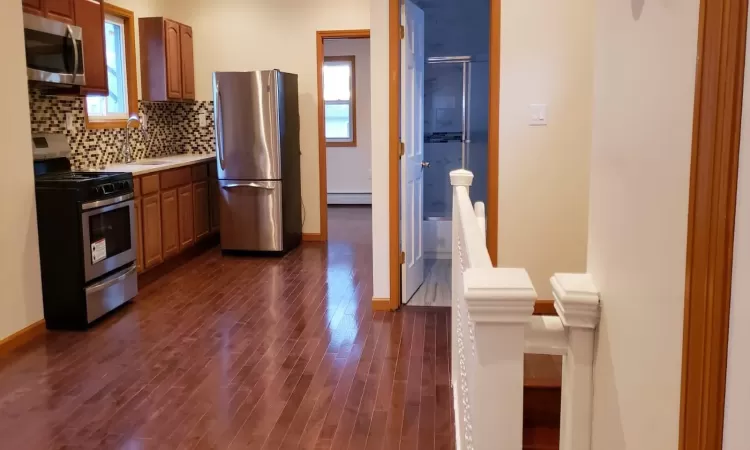 Kitchen/ dinning area featuring decorative backsplash, stainless steel appliances, dark hardwood / wood-style floors, and a baseboard heating unit