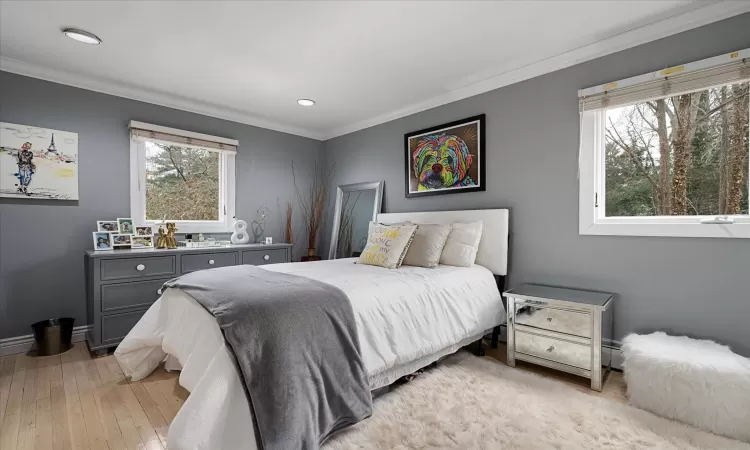 Bedroom with multiple windows, ornamental molding, and light wood finished floors