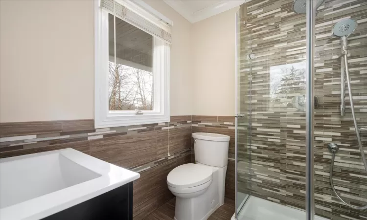 Bathroom featuring a wainscoted wall, toilet, a stall shower, ornamental molding, and tile walls