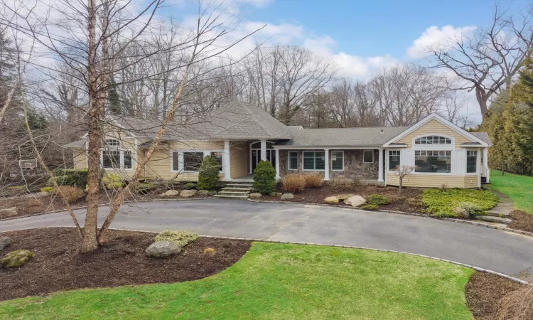 View of front facade with a front yard, stone siding, driveway, and a shingled roof