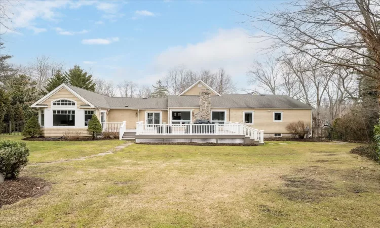 Rear view of house featuring a lawn, fence, and a wooden deck