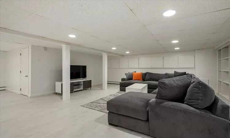 Living room with baseboards, a baseboard radiator, recessed lighting, a paneled ceiling, and light wood-type flooring