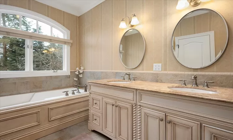 Bathroom featuring a garden tub, ornamental molding, double vanity, and a sink