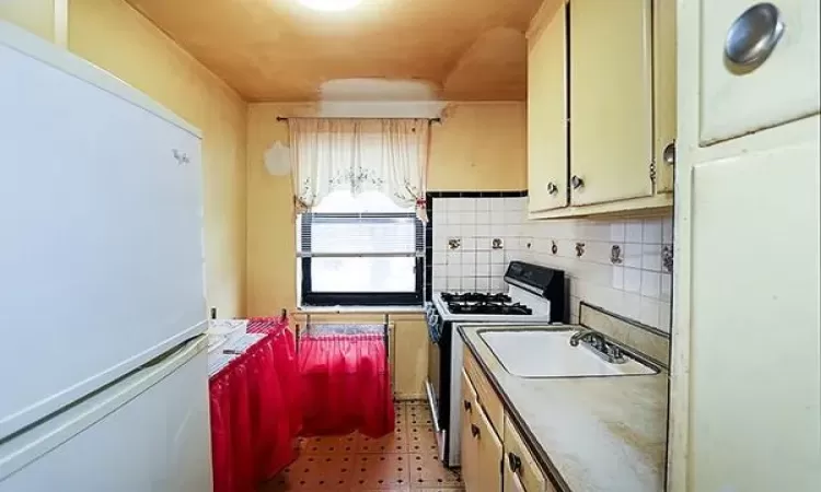 Kitchen with light floors, freestanding refrigerator, a sink, gas range oven, and backsplash