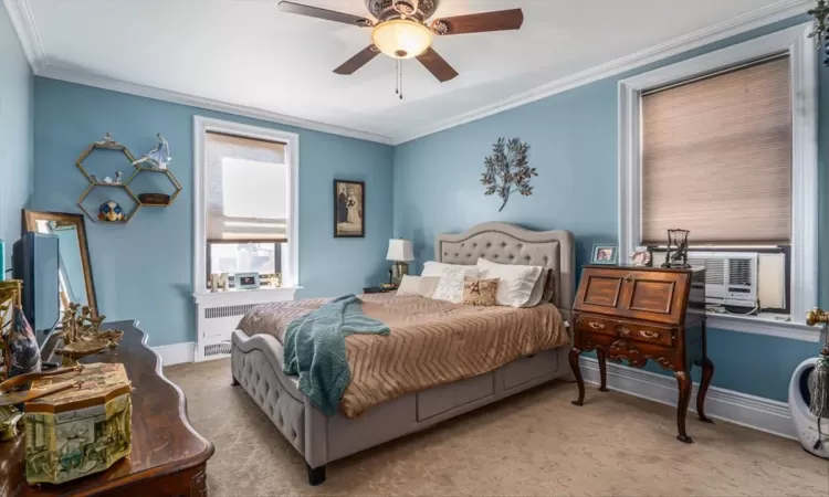 Carpeted bedroom with crown molding, baseboards, radiator heating unit, cooling unit, and a ceiling fan