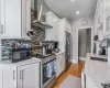 Kitchen with light wood-type flooring, a sink, white cabinetry, stainless steel appliances, and wall chimney range hood